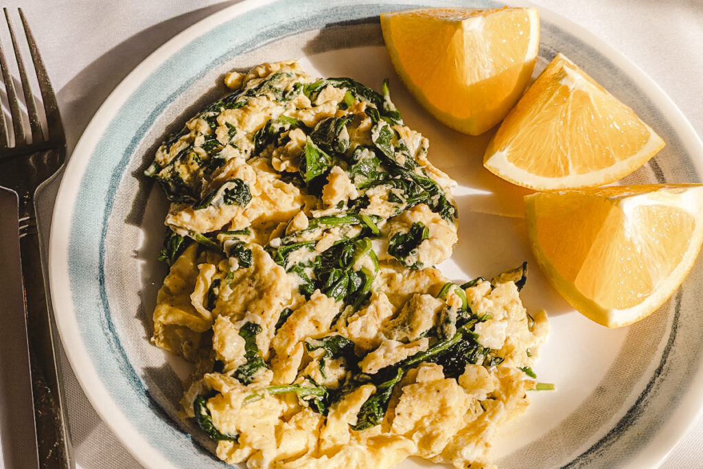 A plate of scrambled eggs with spinach and three orange wedges.