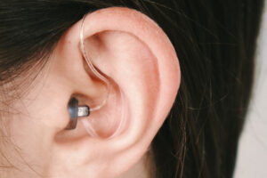A hearing aid in white woman’s ear with wire tube and retaining clip