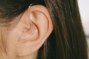 Hearing aid tubing and retention clip visible in a brunette woman’s ear