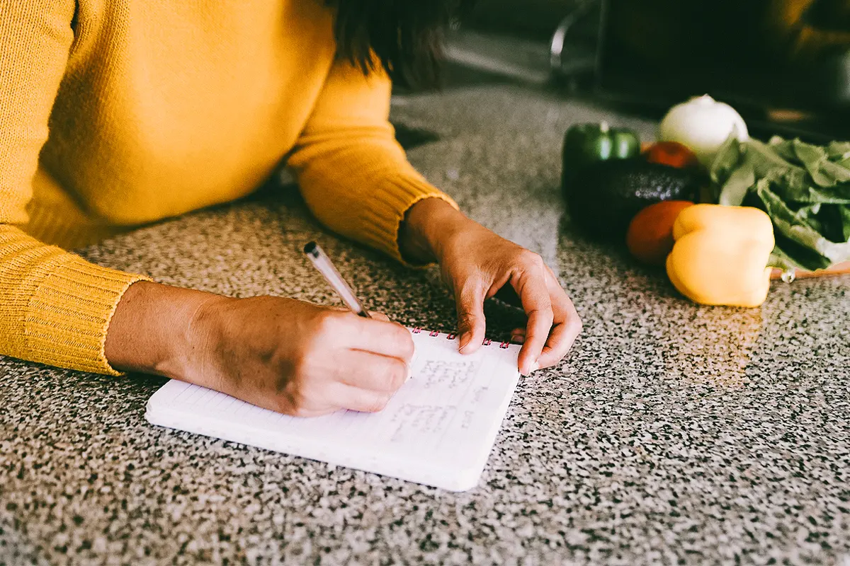 woman writing down ingredients at home in kitchen