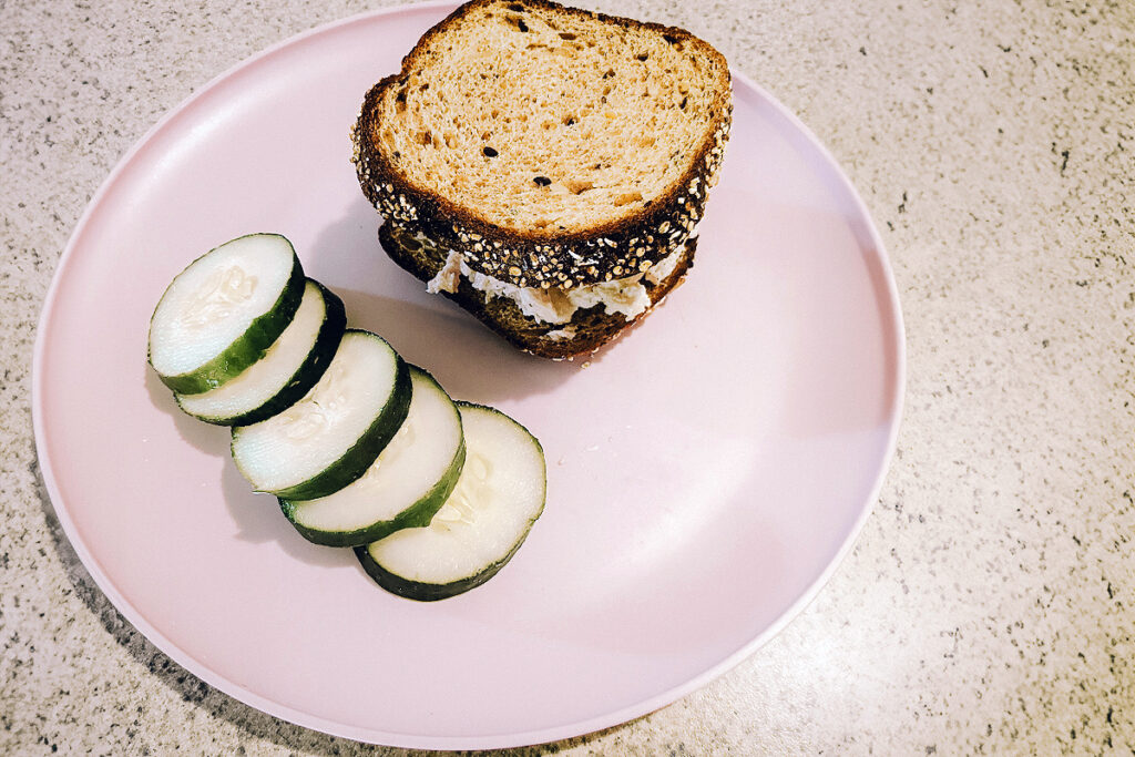 A plate with a tuna sandwich and cucumbers