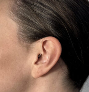 A person with brown hair wears a Jabra Enhance 300 hearing aid