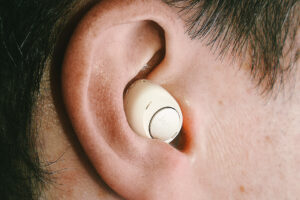 Beige earbud-style hearing aid nestled in a white man’s ear bowl.