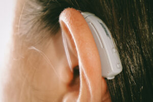 Gray behind-the-ear hearing aid worn by a brunette woman