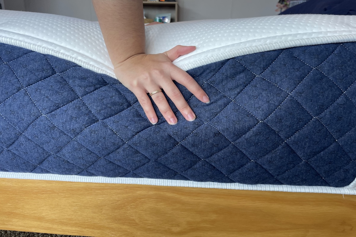 A hand pressing down on the edge of a blue and white Brooklyn Bedding Signature mattress