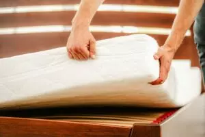 Man’s hands lifting a mattress from a platform base