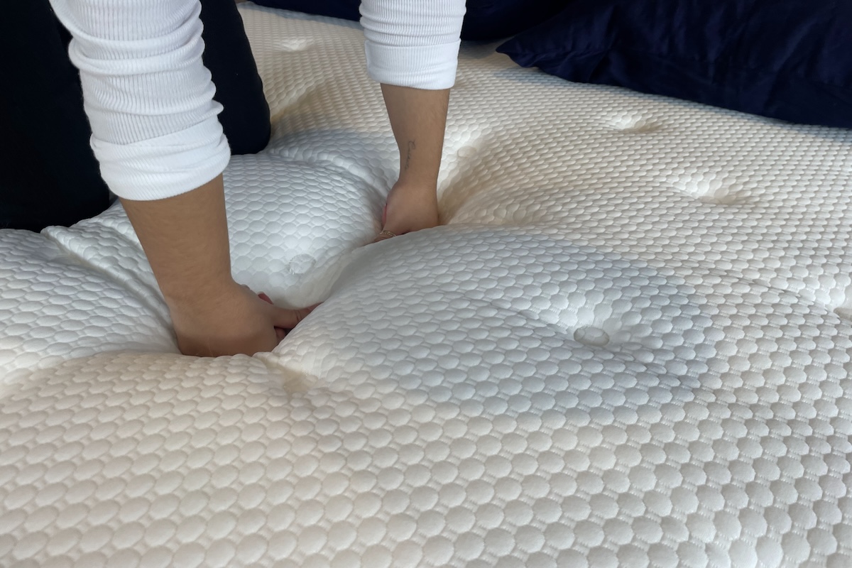 One of our testers kneels on the Nolah Original mattress and presses her fists into the material