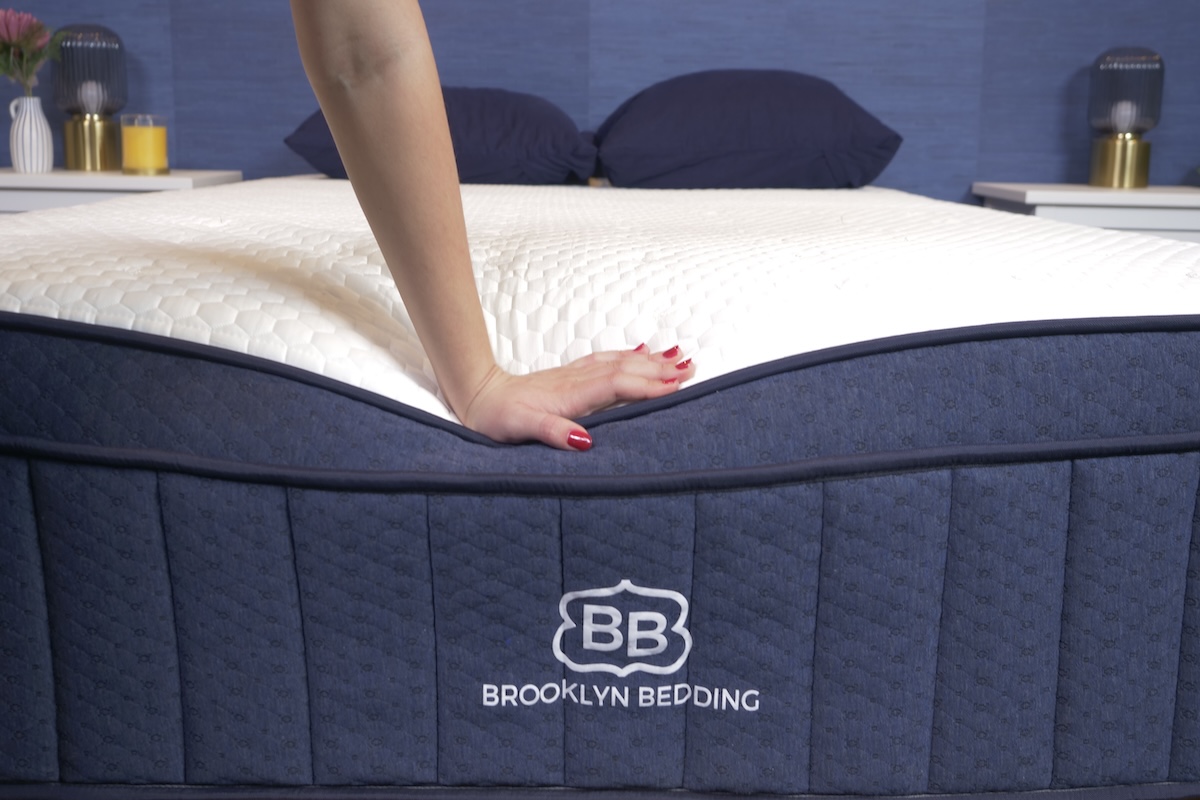 A hand pushes down on the edge of a Brooklyn Bedding mattress