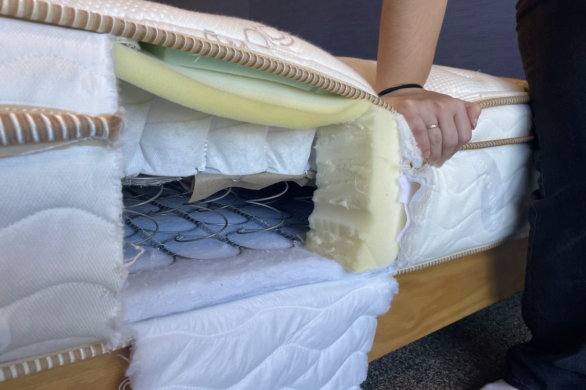 A hand presses down on the edge of the mattress next to an opening that shows the interior mattress composition of coils and foam