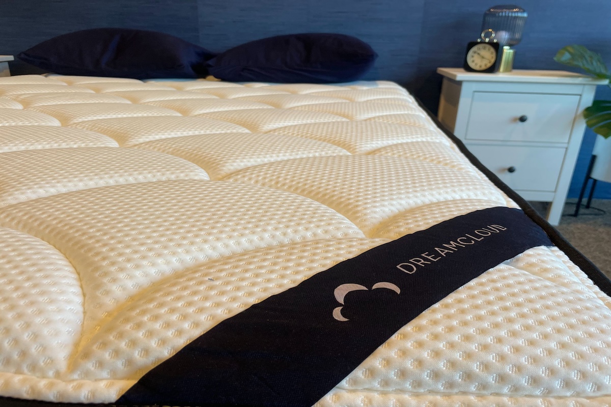 An unmade DreamCloud Memory Foam mattress with blue pillows