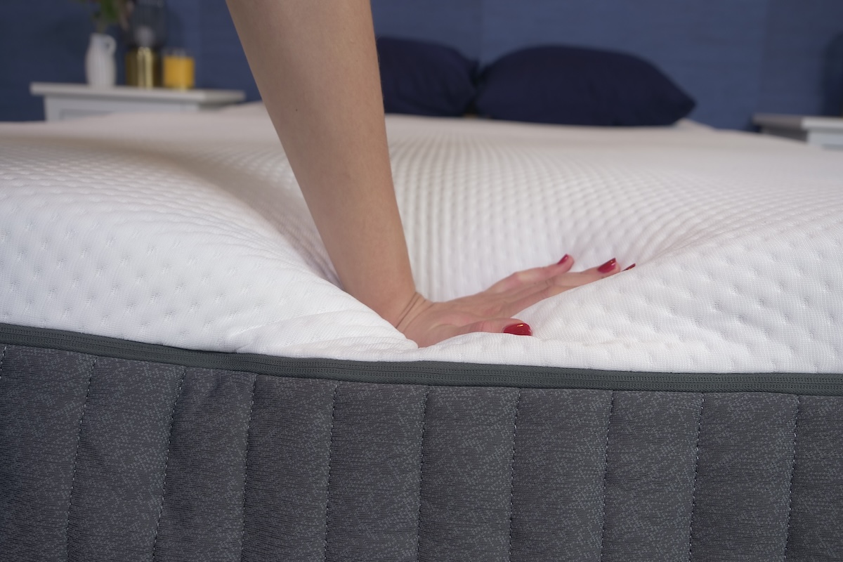 Woman’s hand pushing down on the edge of a mattress
