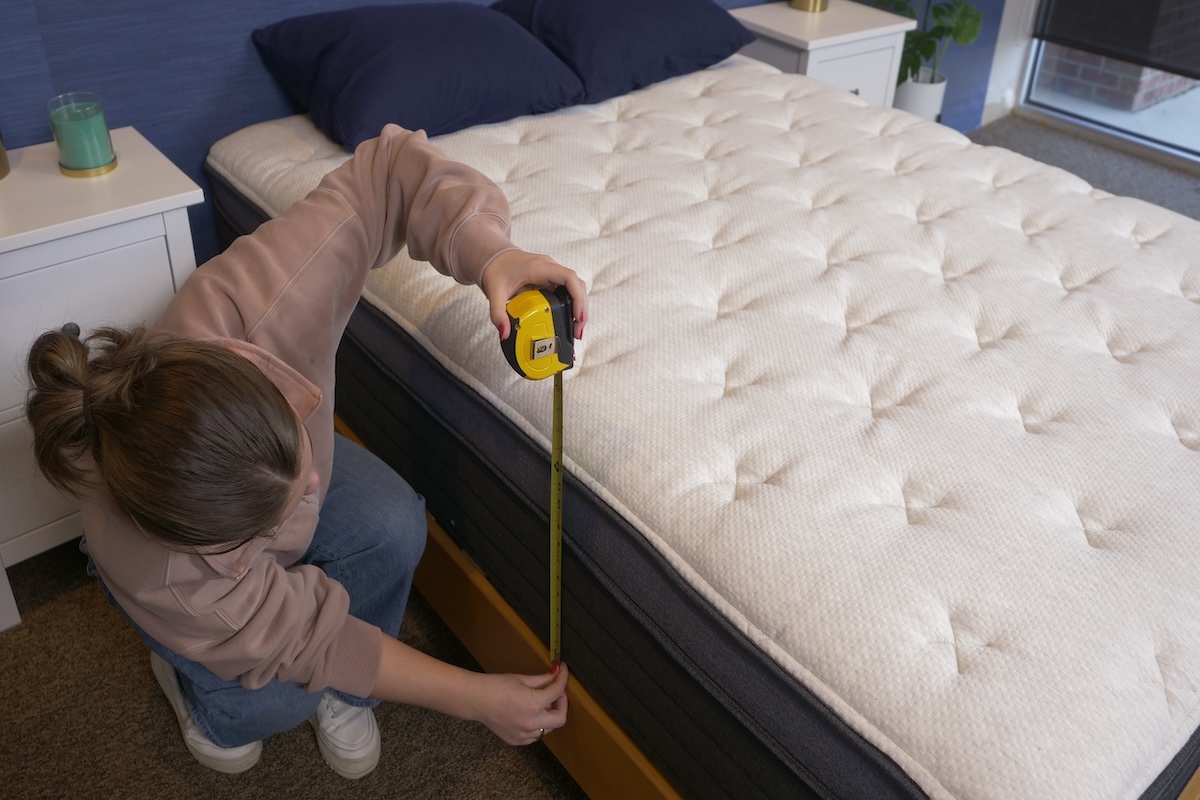 A woman uses a measuring tape to measure the height and thickness of a Helix mattress]