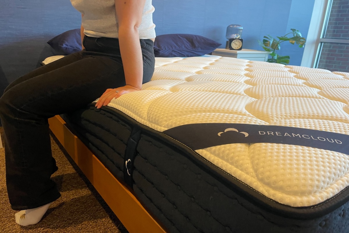 A woman sits on the DreamCloud Premier Hybrid Mattress to test for edge strength