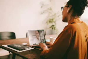 Woman sitting at table talking to a man via a video call on her computer.