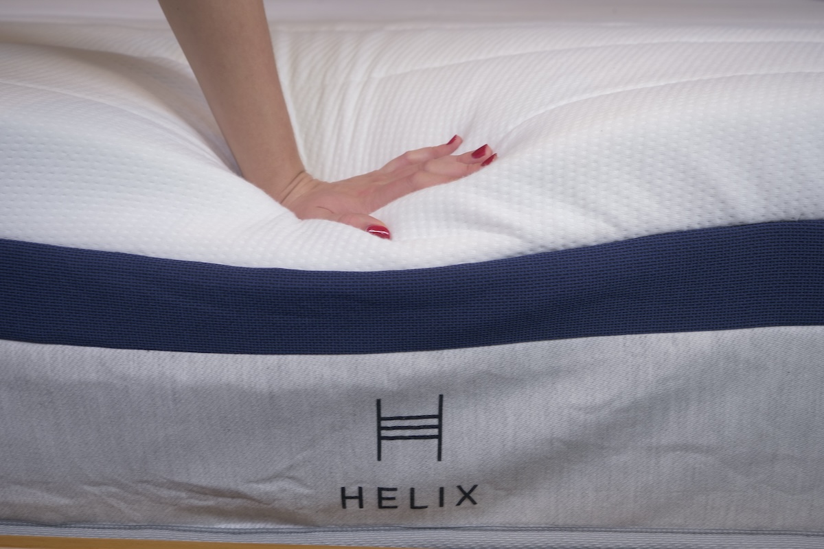  A woman’s hand pushes down on the edge of the Helix Midnight mattress