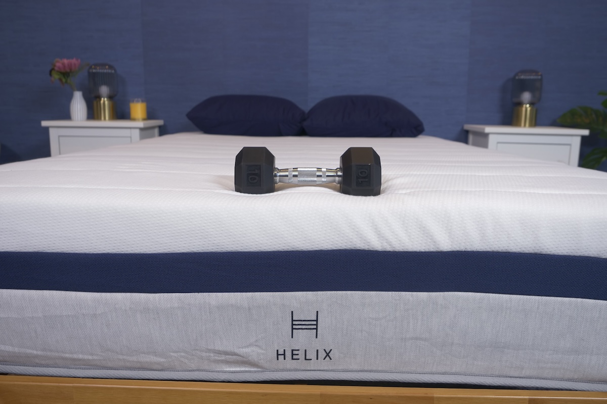 A 10-pound dumbbell rests on top of a Helix Midnight mattress to demonstrate the firmness of the mattress