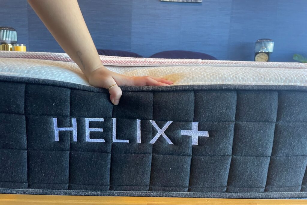 Hand pressing down on the edge of the Helix Plus mattress