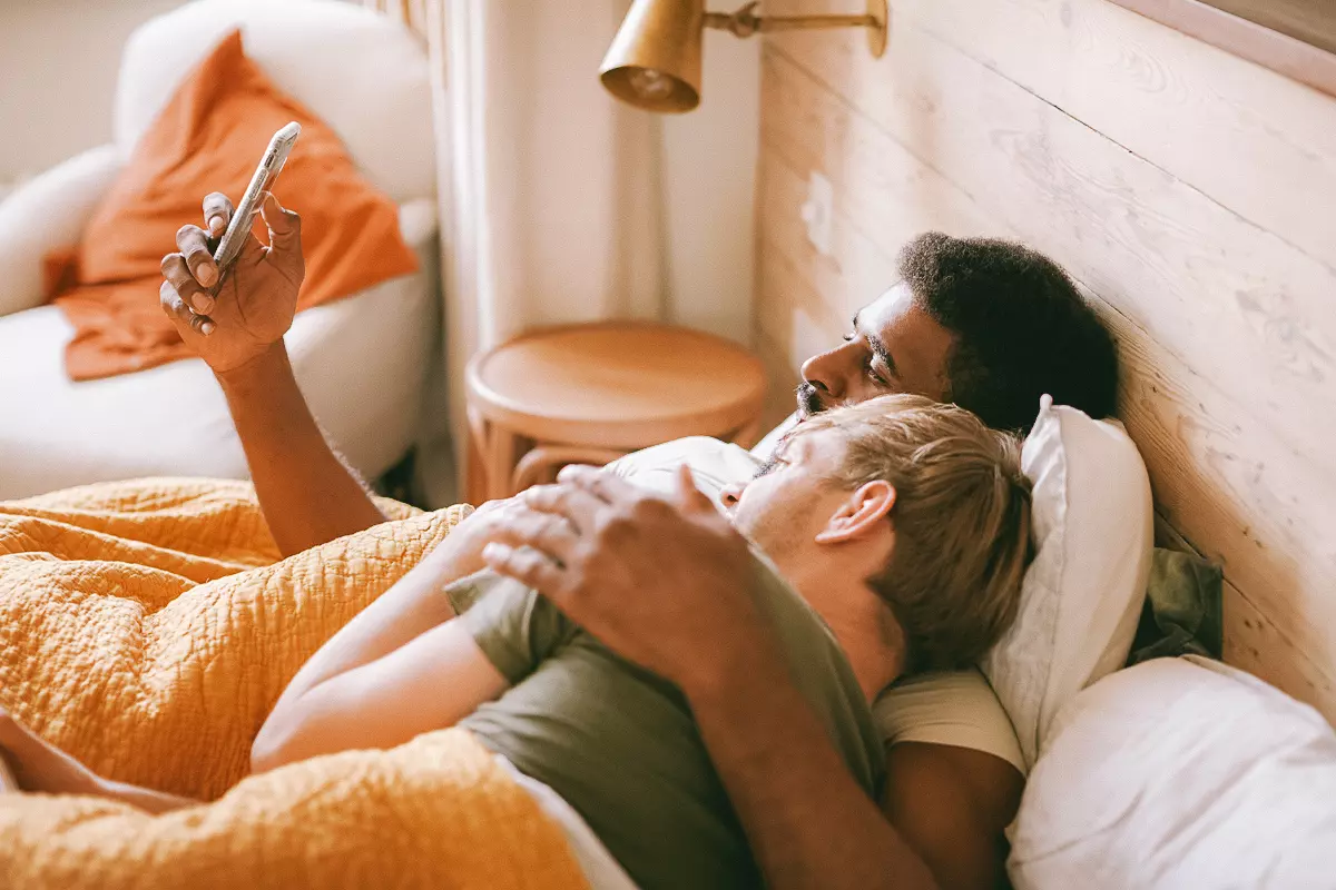 Two people lying in bed scrolling through a phone