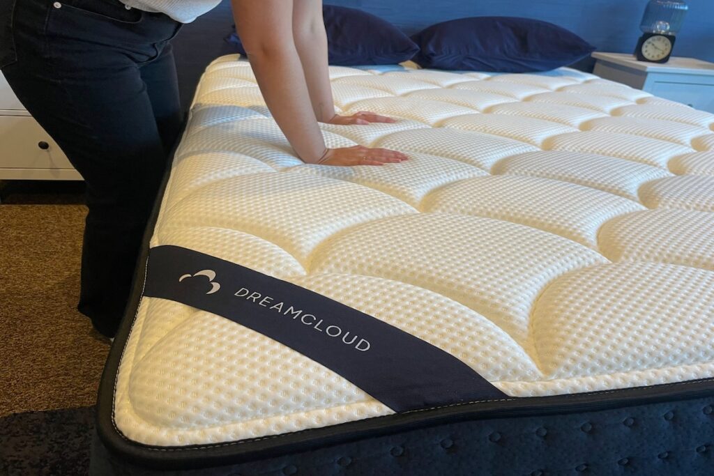 Woman bends over the DreamCloud Hybrid Mattress and pushes down