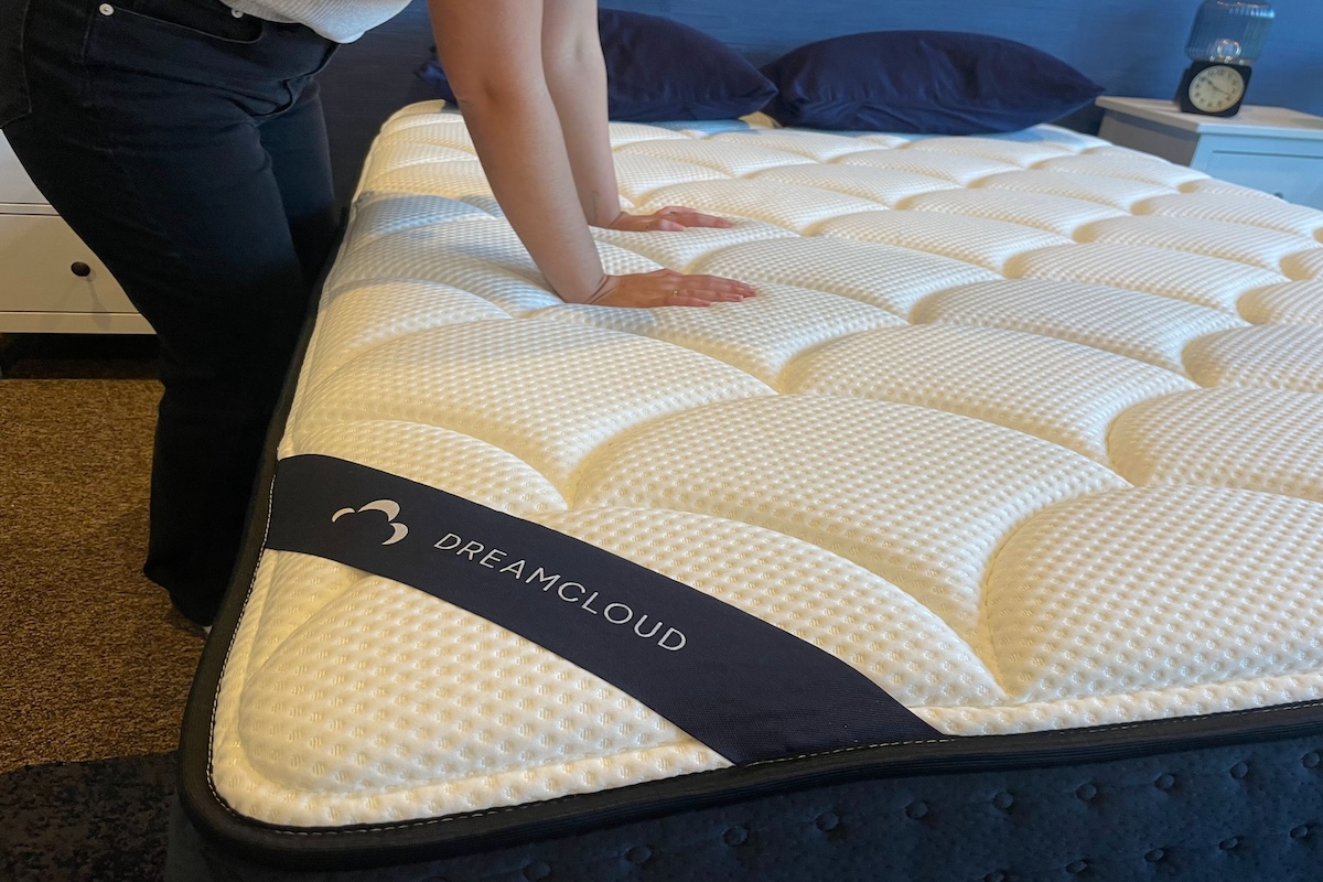 A woman presses down on the top of the DreamCloud Memory Foam mattress. 