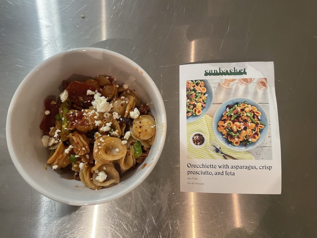 Bowl of orecchiette sprinkled with feta cheese and a recipe card next to it