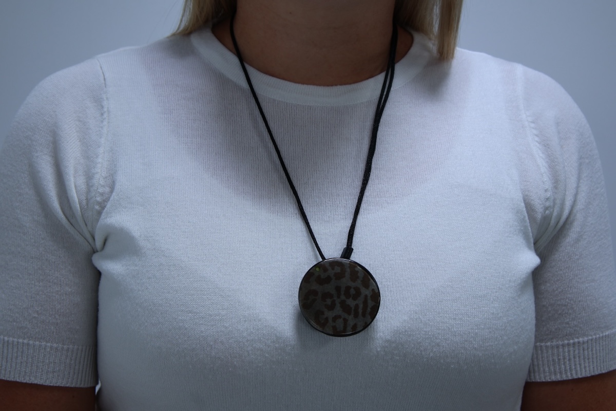 Woman wears medical alert help button necklace around her neck with a Bella Charm over the top