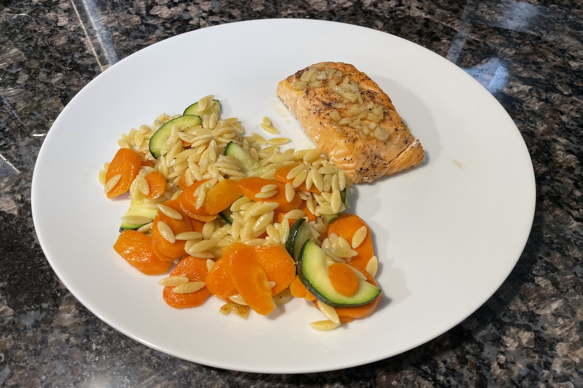 Cooked lemon ginger salmon with orzo, carrots, and zucchini on a white plate
