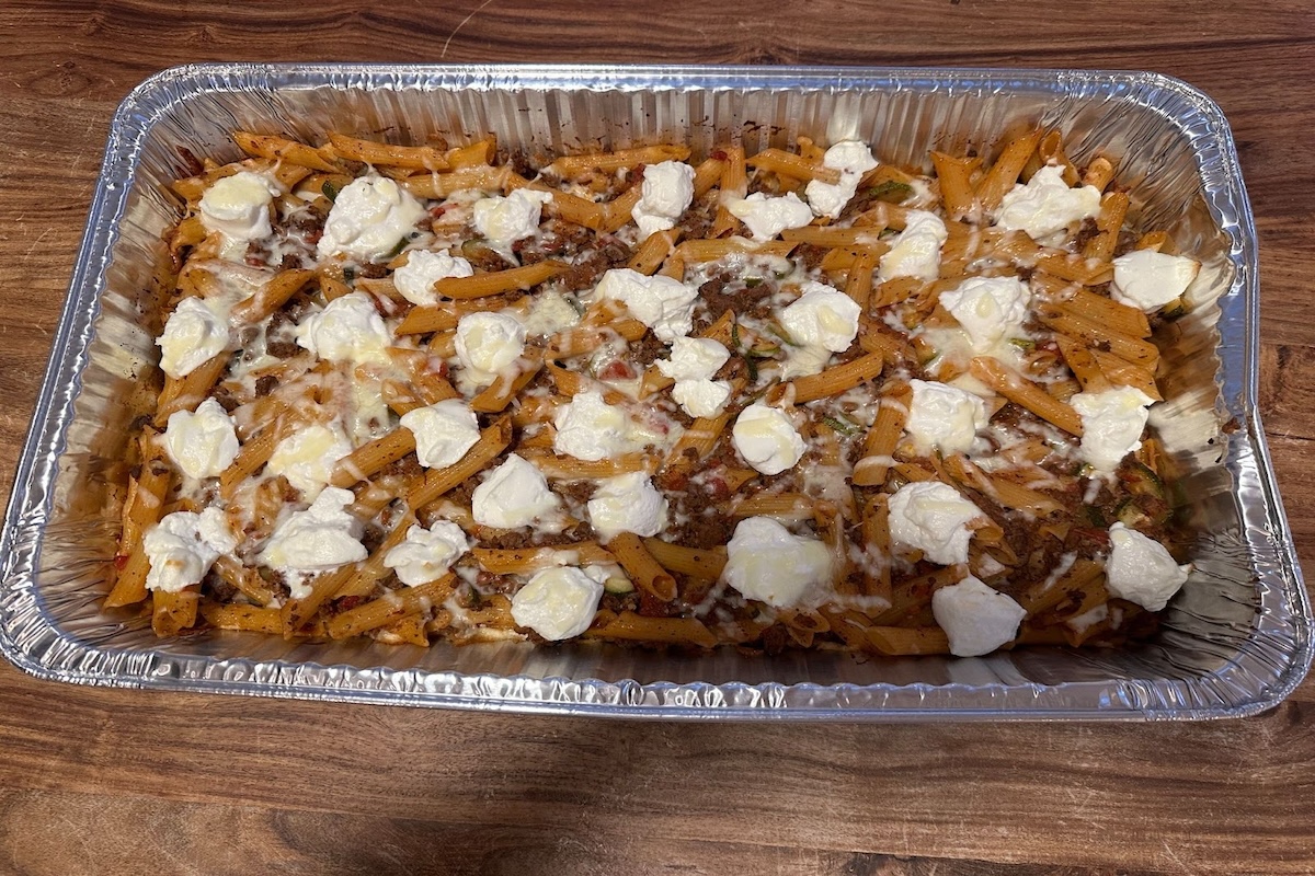 Beef and penne pasta casserole with dollops of ricotta cheese on top in an aluminum baking pan.