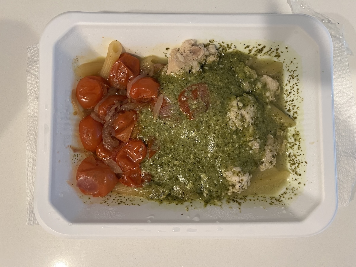 A cooked Trifecta meal with chicken breast, pesto, and tomatoes in a disposable serving dish.