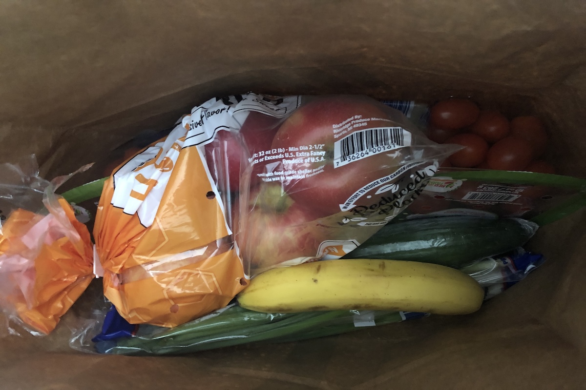 Apples, cherry tomatoes, cucumbers, and one banana inside a brown paper grocery bag.