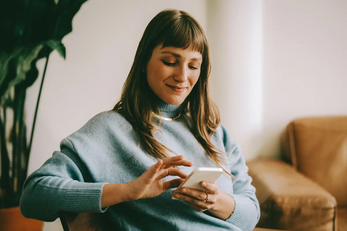 A woman smiles as she interacts with her mobile phone.