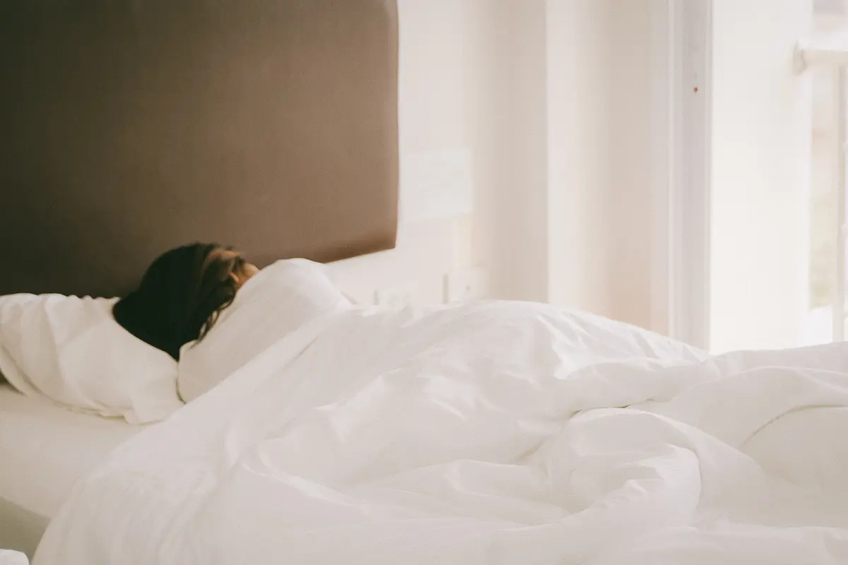 A woman sleeps with her back to the camera in a bed with a white comforter and sheets.