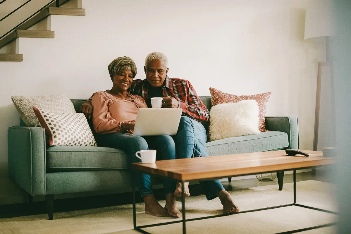 man and woman smile on couch while looking at laptop