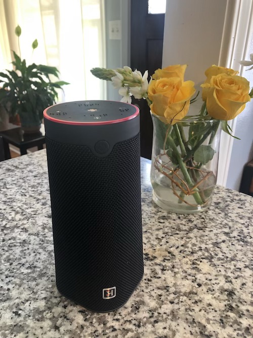 The WellBe Medical Alert Speaker on a countertop next to some yellow roses in a vase.