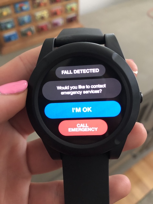 A woman’s hand holds the WellBe Medical Alert Watch showing the digital screen