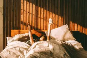 woman raises her hands happily as she wakes up in bed