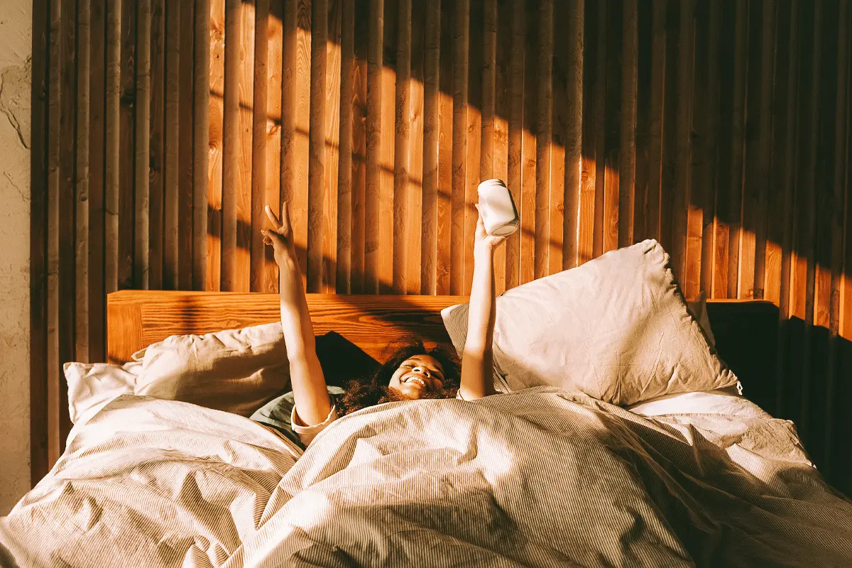 woman raises her hands happily as she wakes up in bed