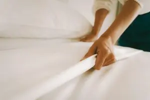 woman makes the bed by smoothing the sheets