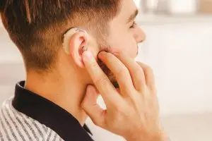 young man touches hearing aid in his right ear