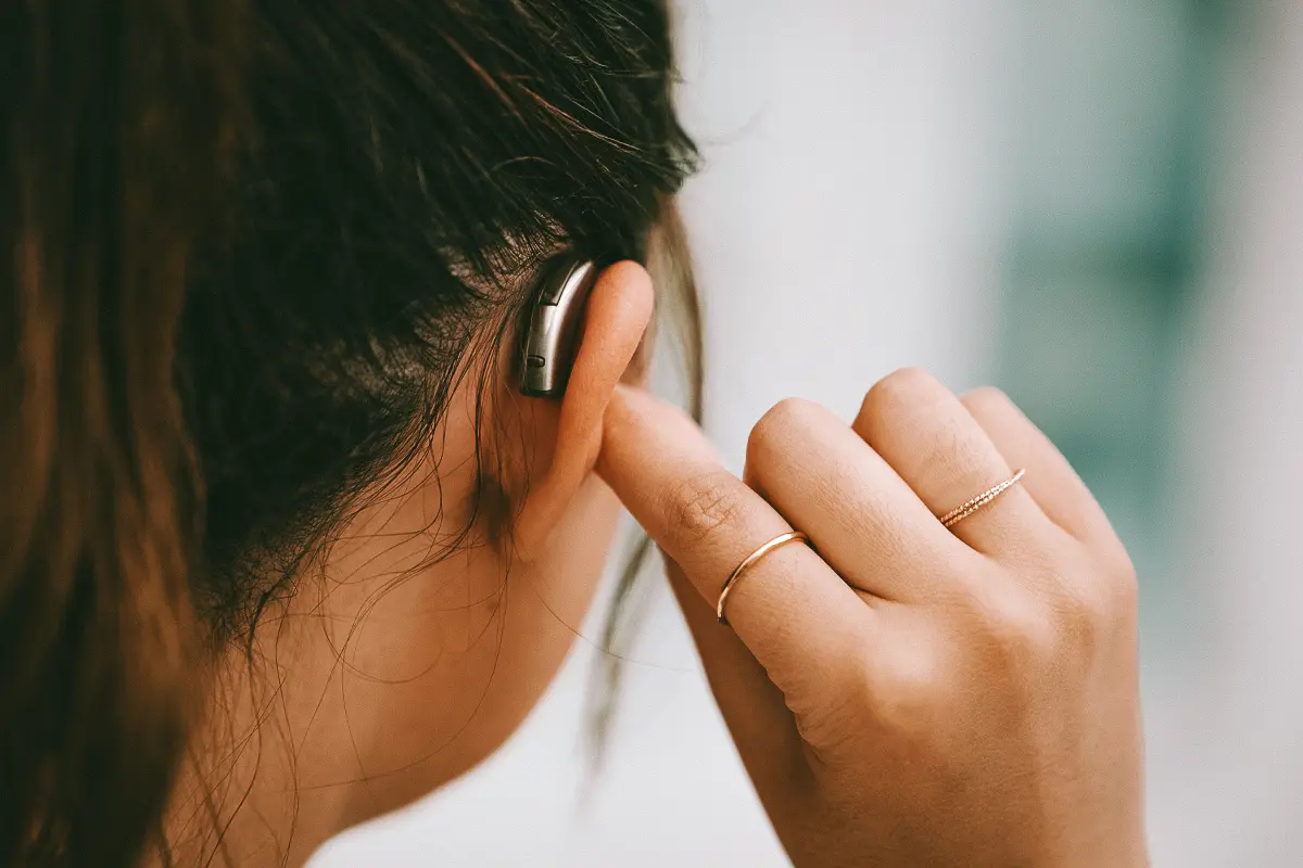 Woman taps a hearing aid she's wearing in her right ear