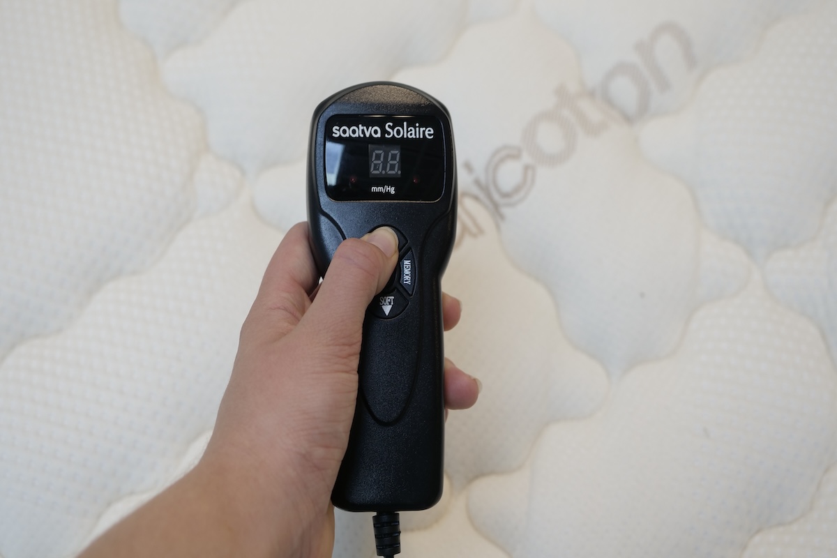 One of our testers holding the Saatva Solaire remote above the mattress.